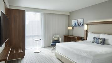 A hotel room with a large bed, a TV, a desk, a chair, and a window with curtains.