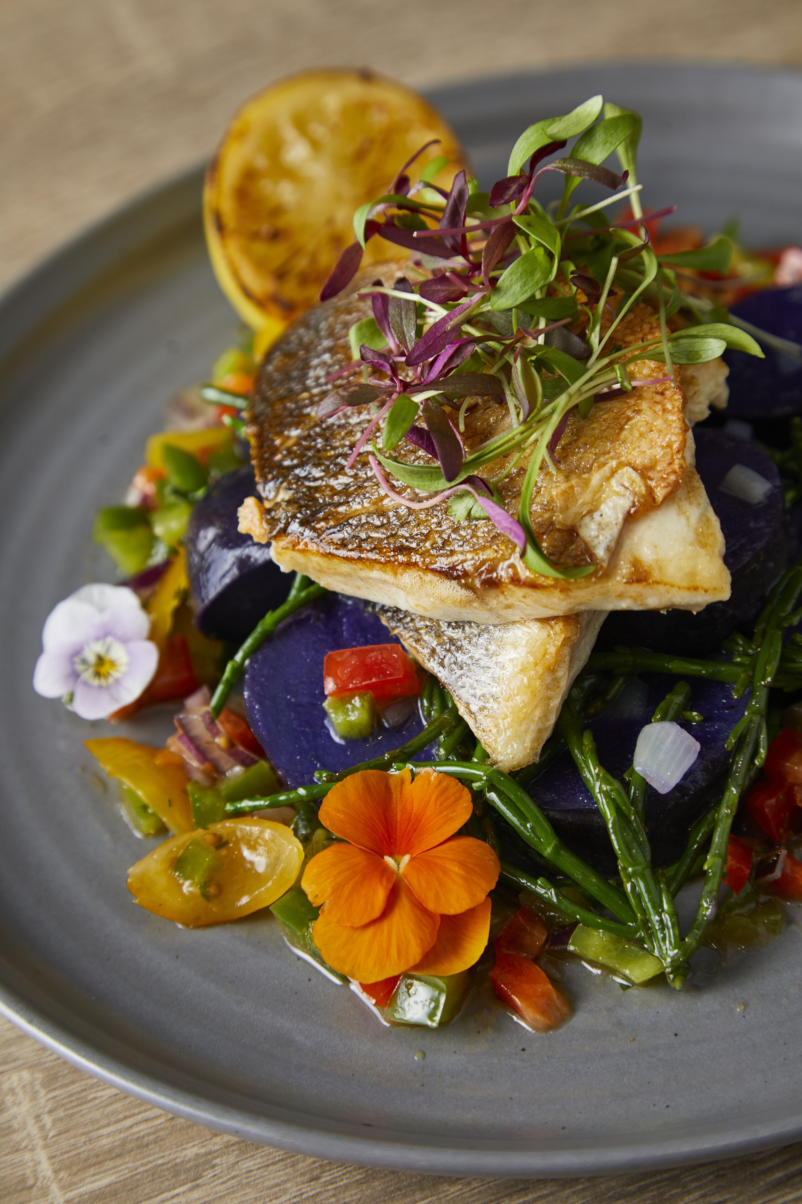 A plate of food with a piece of fish, vegetables, and a lemon slice.