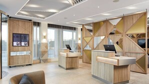 Una moderna zona de recepción con mostradores de madera, una gran pantalla digital y un área de descanso confortable.