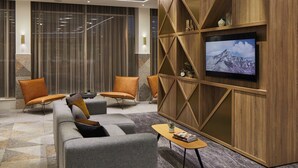 Un vestíbulo moderno con un sofá, dos sillones, una mesita de café y un televisor montado en una pared de madera.