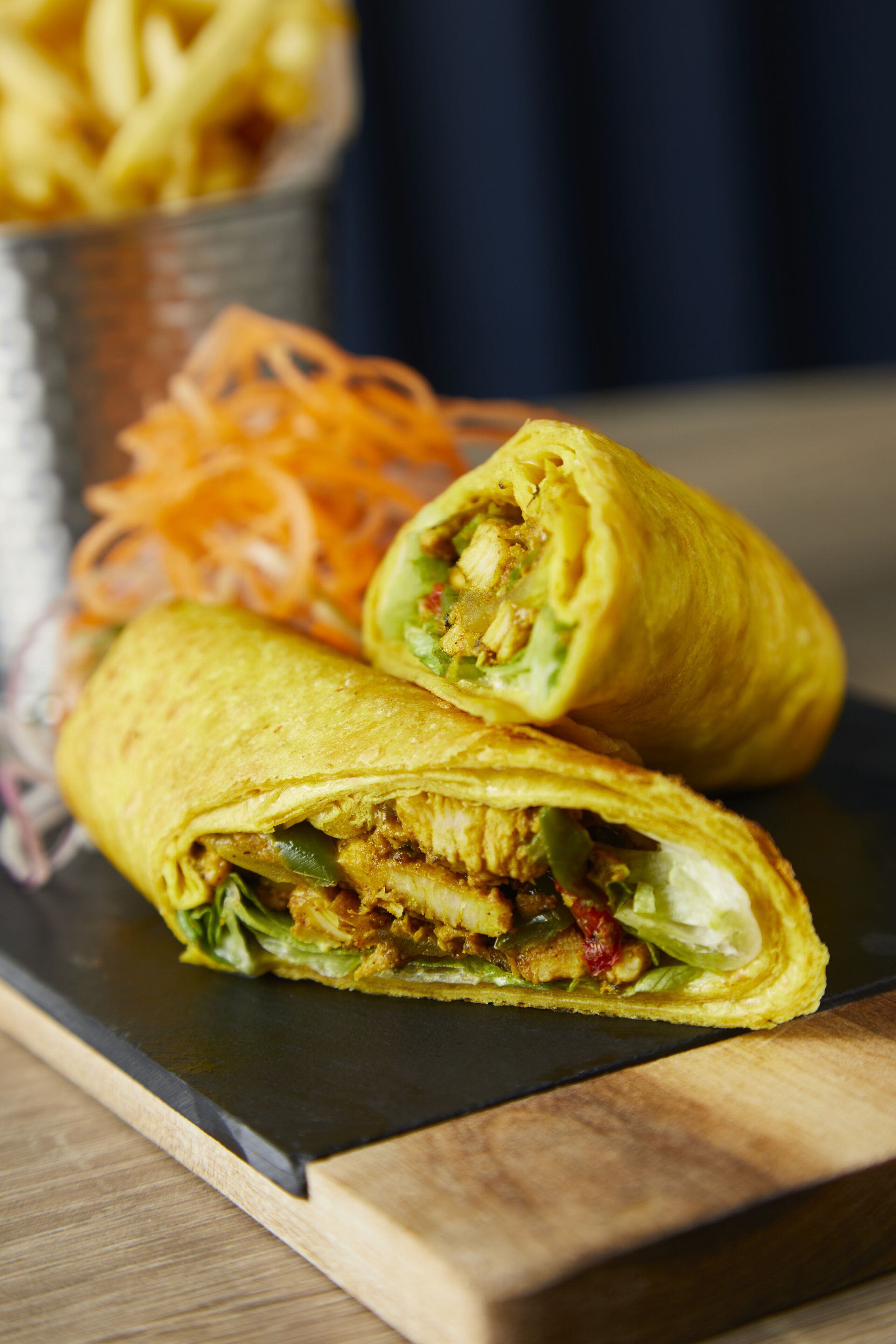 A burrito cut in half with visible fillings, served on a black plate with a side of shredded carrots.