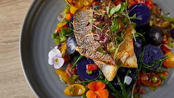 A plate of food with a fish fillet, vegetables, and edible flowers.