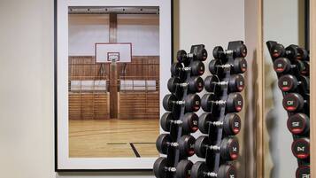 A gym with a basketball court and a wall-mounted rack of dumbbells.
