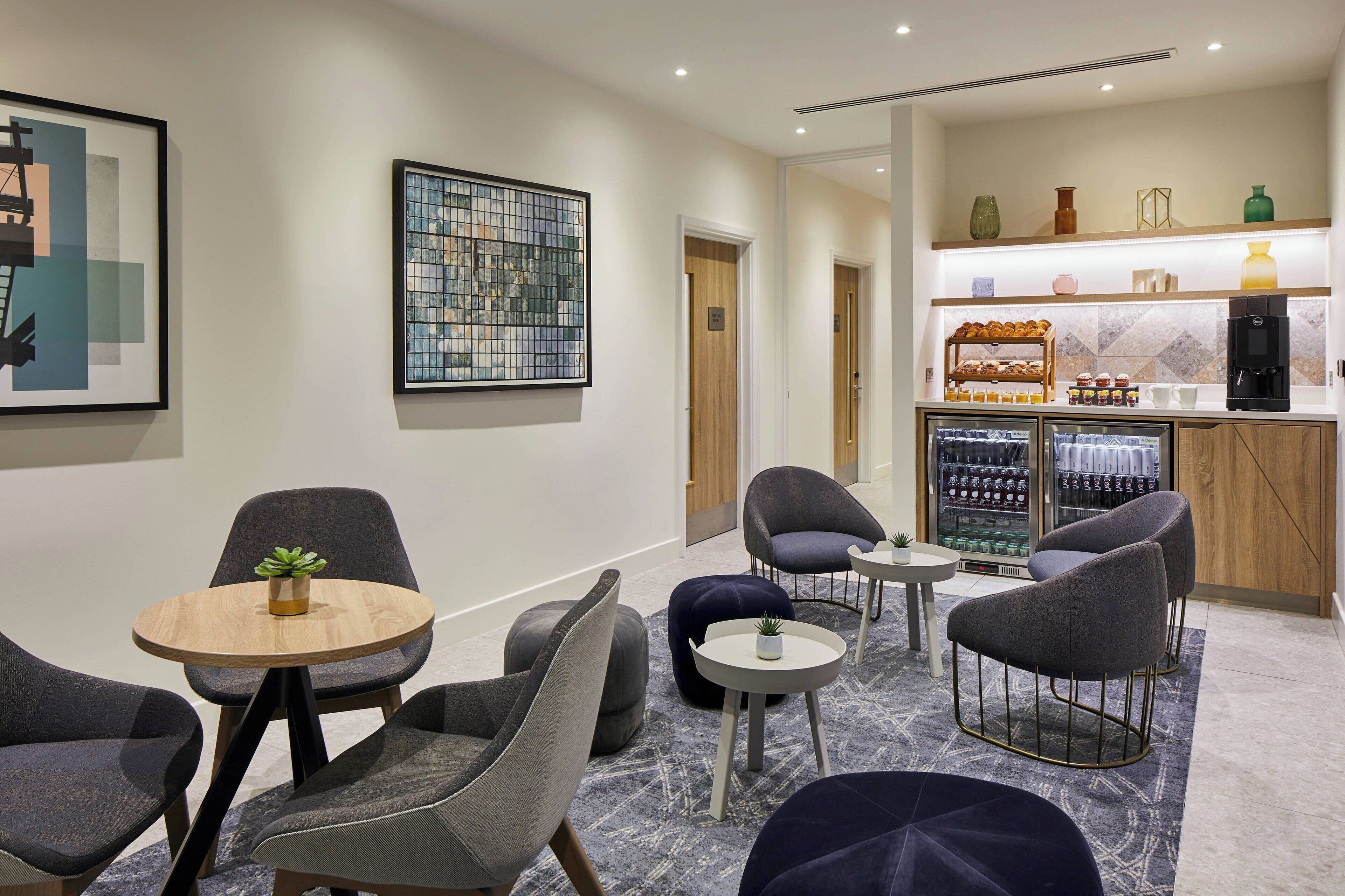 A modern lounge area with seating, a coffee station, and artwork on the walls.
