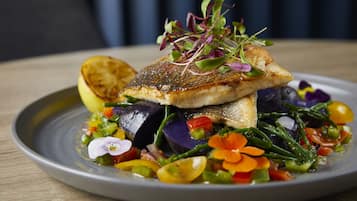Ein Teller Essen mit einem Fischstück, Gemüse und einer Zitronenscheibe.