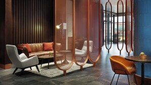 A modern hotel lobby with a leather sofa, a white armchair, a round table, and a blue-tiled wall. - Four Points by Sheraton Prishtina City (Preoce)