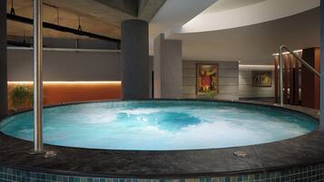 A modern indoor swimming pool with a tiled edge, a metal ladder, and a wall-mounted painting.