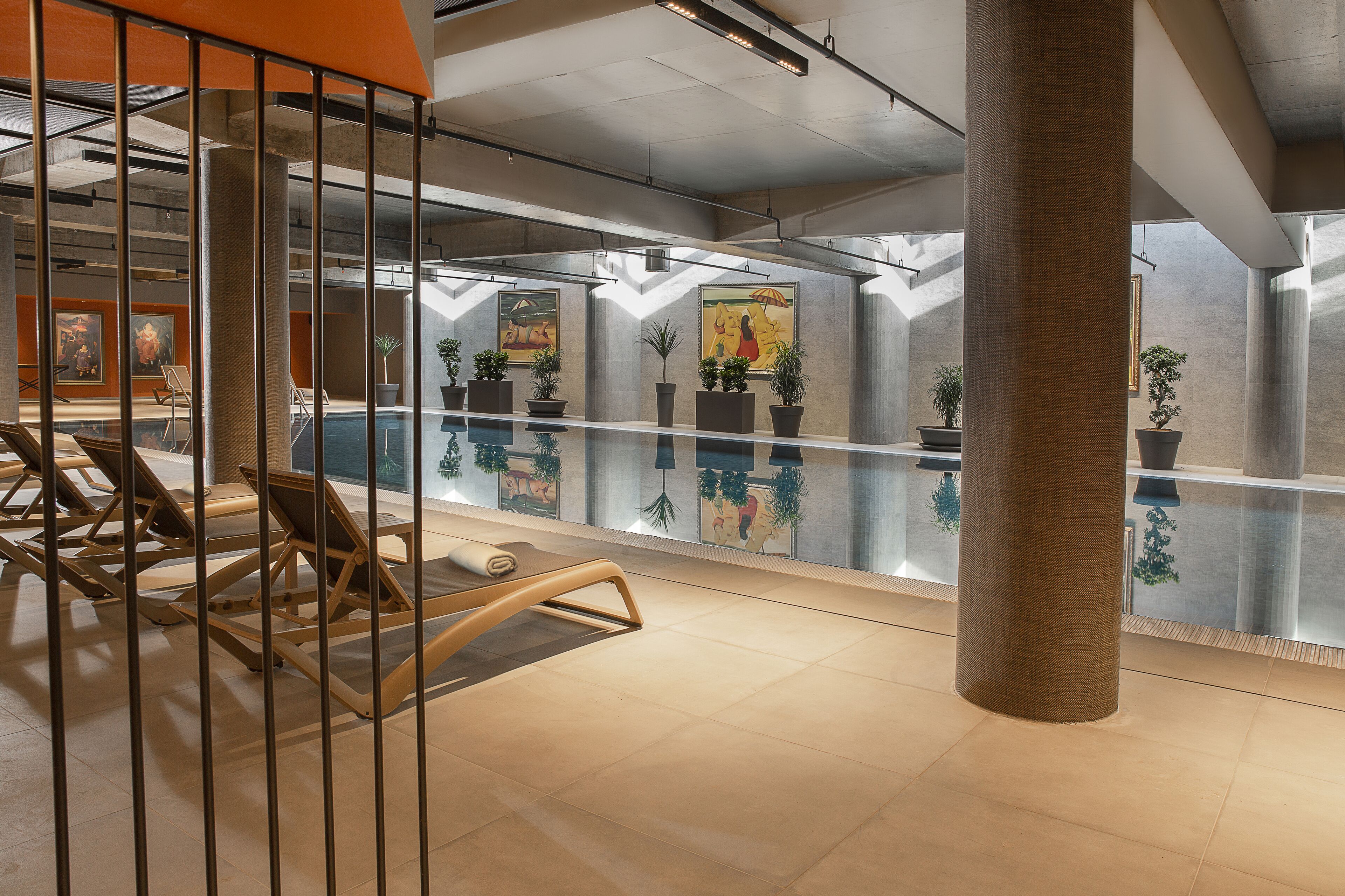 A modern indoor pool area with lounge chairs, potted plants, and artwork on the walls.