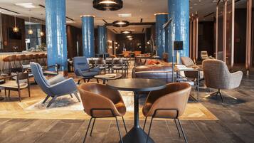 Un hall d’hôtel moderne, doté de hauts plafonds, de colonnes cylindriques bleues, de sièges en cuir et d’un espace bar.