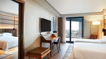 A hotel room with two beds, a desk, a chair, a TV, and a view of the city.