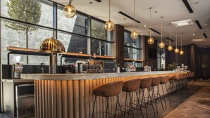 A modern bar area with a long counter, multiple stools, and pendant lighting. - Four Points by Sheraton Prishtina City (Preoce)