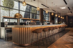 A modern bar area with a long counter, multiple stools, and pendant lighting.