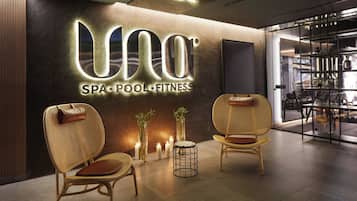 Interior de un spa con piscina y gimnasio, con sillones de mimbre, velas y un letrero moderno.