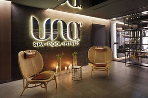 Interior de un spa con piscina y gimnasio, con sillones de mimbre, velas y un letrero moderno.