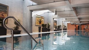 A large indoor swimming pool with clear glass walls, potted plants, and artwork on the walls. - Four Points by Sheraton Prishtina City (Preoce)