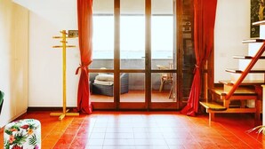 A room with a wooden staircase, a sliding glass door leading to an outdoor seating area, and a small table with a floral tablecloth. - Altramonto House (Siracusa)