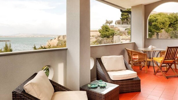 A balcony with wicker furniture, a small table, and a view of the sea. - Altramonto House (Siracusa)
