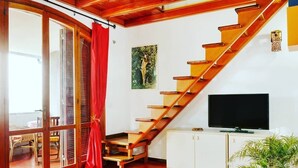 A living room with a wooden staircase, a television, a cabinet, and a potted plant. - Altramonto House (Siracusa)