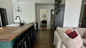 Une cuisine dotée d’un plan de travail en bois, de tabourets de bar noirs et d’un lustre suspendu.