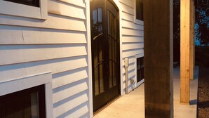 Une maison avec une porte d’entrée noire, un revêtement extérieur blanc et un porche en béton.