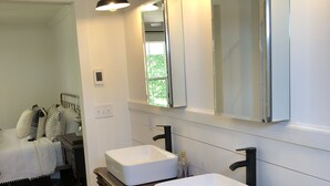 Une salle de bain avec deux lavabos blancs, un meuble-lavabo en bois, un grand miroir et trois appliques murales.