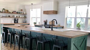 Une cuisine moderne dotée d’un grand îlot central, de tabourets de bar et offrant une vue sur l’extérieur.