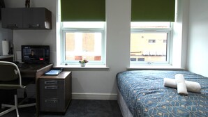A bedroom with a desk, computer, and a bed with a patterned bedspread. - Victoria House - Classic Studio by CovStays (Coventry)