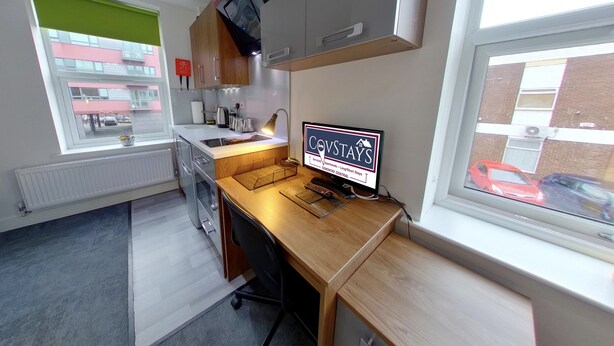 A compact kitchen with a wooden countertop, a built-in oven, and a window with a view of the street. - Victoria House - Classic Studio by CovStays (Coventry)