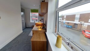 A modern kitchen with a wooden countertop, a yellow mug, and a window with a view of a red car and buildings. - Victoria House - Classic Studio by CovStays (Coventry)