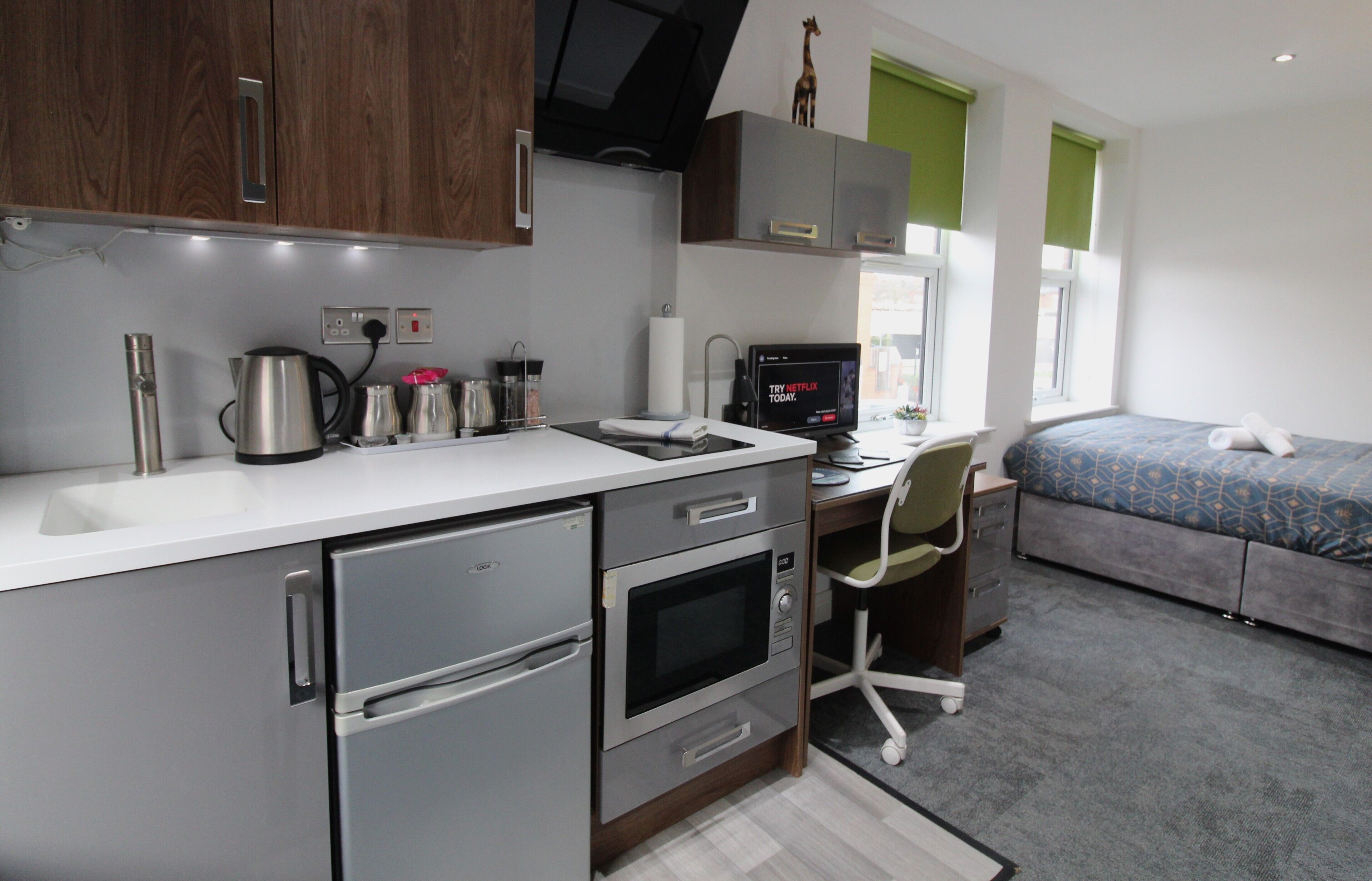 A compact hotel room with a kitchenette, a bed, a desk, and a computer.