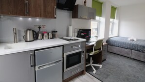 A compact hotel room with a kitchenette, a bed, a desk, and a computer. - Victoria House - Classic Studio by CovStays (Coventry)