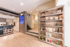 A modern hotel lobby with a reception desk, a staircase, and a bookshelf with various items. - Hanting Hotel (Shanghai)