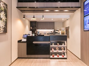 A modern reception desk with a digital display, a coffee machine, and a shelf with potted plants. - Hanting Hotel (Shanghai)