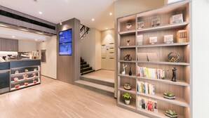 A modern hotel lobby with a reception desk, a staircase, and a bookshelf with various items. - Hanting Hotel (Shanghai)