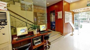 A reception desk with computers, a plant, and a staircase leading to an upper floor. - Hanting Hotel (Shanghai)