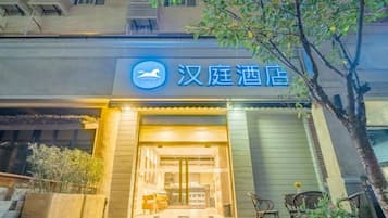 Entrada de hotel com uma placa em caracteres chineses, uma bicicleta estacionada e uma árvore em primeiro plano.