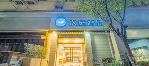 A hotel entrance with a sign in Chinese characters, a bicycle parked outside, and a tree in the foreground. - Hanting Hotel (Shanghai)