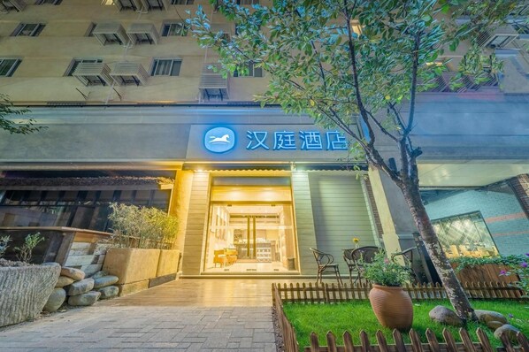 A hotel entrance with a sign, a paved pathway, a wooden fence, and a tree. - Hanting Hotel (Shanghai)