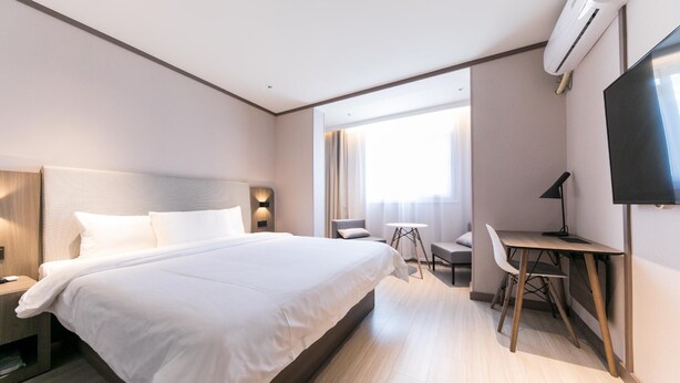 A modern hotel room with a large bed, a desk, a chair, and a TV. - Hanting Hotel (Shanghai)
