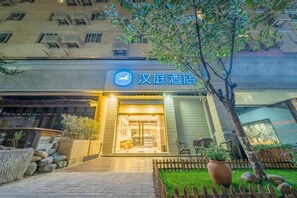 A hotel entrance with a sign, a paved pathway, a wooden fence, and a tree. - Hanting Hotel (Shanghai)