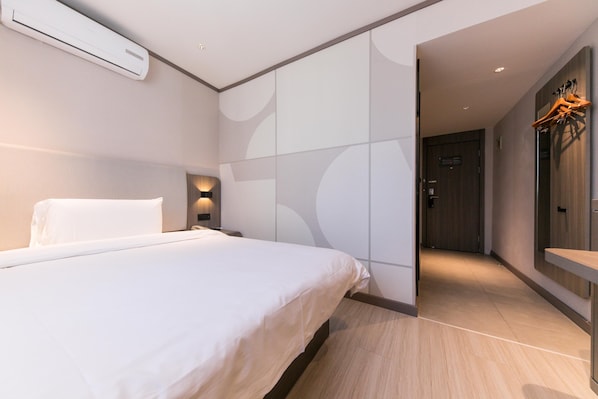 A modern hotel room with a large bed, a wardrobe, and a mirror with clothes hanging. - Hanting Hotel (Shanghai)
