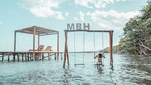 Un conjunto de columpios de madera con las letras 'MBH', un pabellón de madera y sillones de descanso en un muelle.
