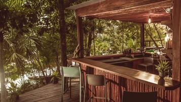 Una terraza de madera con una zona de bar, dos sillas y vistas a un follaje exuberante.