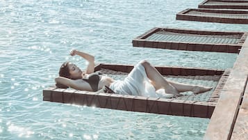 Una persona recostada sobre una plataforma flotante en el agua, con un muelle de madera que se adentra en ella.