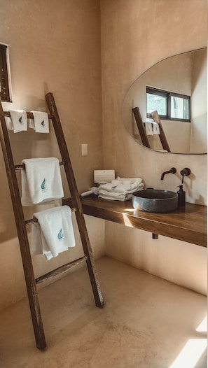 A bathroom with a wooden ladder, a sink with a round basin, a mirror, and towels with a water droplet logo.