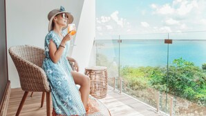 Una mujer sentada en una silla de mimbre en un balcón con vista al mar.