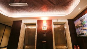An elevator with a digital display and emergency buttons, flanked by marble walls and a wooden ceiling. - Chonpines Hotel (Dalian)