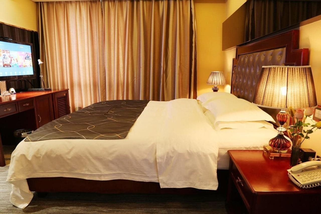 Habitación de hotel con una cama grande, un televisor sobre un escritorio de madera, una lámpara y un teléfono en una mesita de noche de madera.