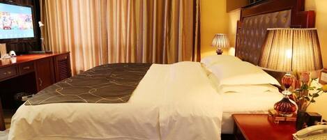 Habitación de hotel con una cama grande, un televisor sobre un escritorio de madera, una lámpara y un teléfono en una mesita de noche de madera.