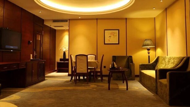 A hotel room with a large circular ceiling light, a television, a sofa, a chair, and a small table. - Chonpines Hotel (Dalian)